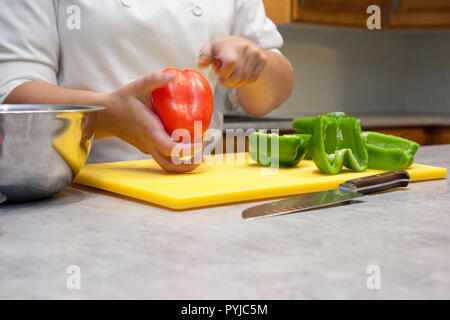 Close up of hands slicing a red bell pepper on a cutting board in the kitchen Stock Photo