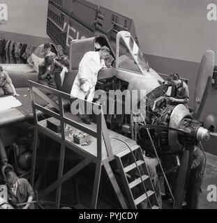 1960s, historical, male engineer in whitecoat supervising a number of young aviaiton apprentices as they work on the cockpit of an aircraft. Stock Photo