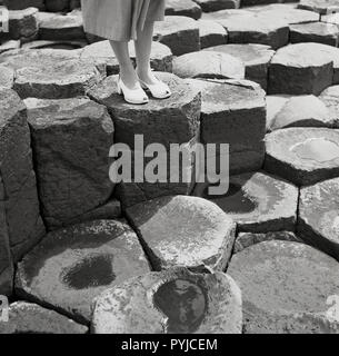 1950s, historical, close-up of a lady's feet standing on one of the ancient hexagonal interlocking basalt column's at the famous Giant's Causeway in Co. Antrim, Northern Ireland, UK. The causeway on the Co. Antrim coast is a spectacular natural wonder, and has an estimated 40,000 such columns resulting from an ancient volcanic fissure eruption. Stock Photo