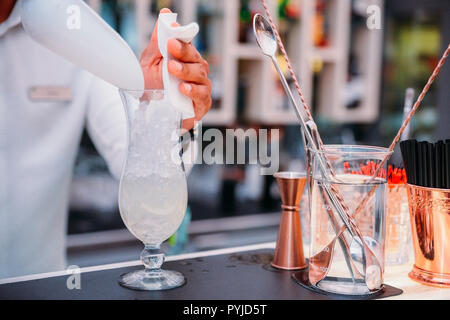 Unidentifiable bartender preparing an alcoholic drink at bar by pouring ice. Measuring instruments on side. Stock Photo