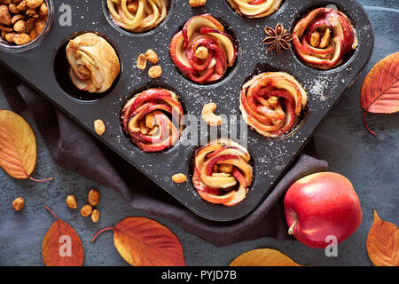 Tray of apple roses baked in puff pastry on gray textured background with Autumn leaves and red apples Stock Photo