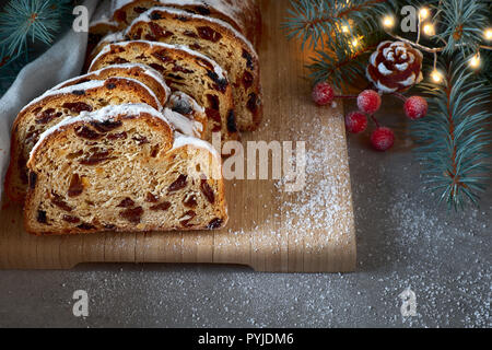 Christmas stollen on darkfestive background with fir twigs, lights and and berries. Close-up on this traditional German dessert for Christmas celebrat Stock Photo