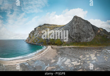 Big sandy aerial drone panorama of Bunes beach in bay surrounded by steep mountains in sunset with dramatic colorful sky and azure sea and big rock in Stock Photo