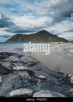 Rocks on beach of fjord of Norwegian sea in winter with snow. Skagsanden beach, with blue sky and clouds in Lofoten islands, Norway. Photo taken in no Stock Photo