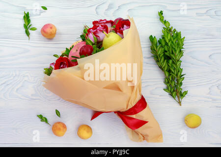 Original bouquet of fruits and flowers lies on a wooden table Stock Photo