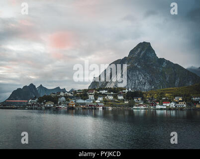 Norwegian fishing village Reine at the Lofoten Islands in Norway. Dramatic sunset clouds moving over steep mountain peaks in dusk. Reflection of stree Stock Photo