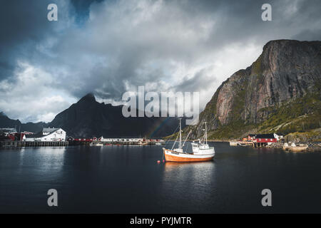 Reine, September 2018: Ship with rainbow in the background in the harbour of famous tourist attraction of Reine in Lofoten. Photo taken in Norway. Stock Photo