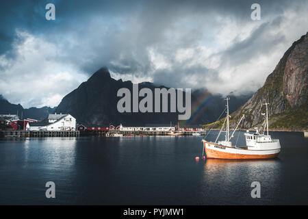 Reine, September 2018: Ship with rainbow in the background in the harbour of famous tourist attraction of Reine in Lofoten. Photo taken in Norway. Stock Photo