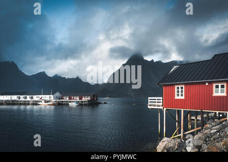 Rainbow ofer red houses rorbuer of Reine in Lofoten, Norway with red rorbu houses, clouds, rainy blue sky and sunny. Bridges and mountains in the back Stock Photo