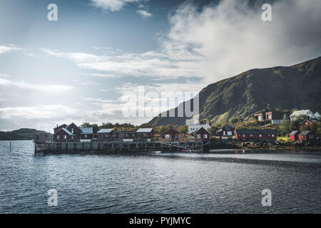 Rainbow ofer red houses rorbuer of Reine in Lofoten, Norway with red rorbu houses, clouds, rainy blue sky and sunny. Bridges and mountains in the back Stock Photo