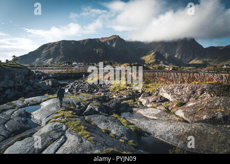 Rainbow ofer red houses rorbuer of Reine in Lofoten, Norway with red rorbu houses, clouds, rainy blue sky and sunny. Bridges and mountains in the back Stock Photo