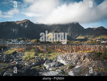 Rainbow ofer red houses rorbuer of Reine in Lofoten, Norway with red rorbu houses, clouds, rainy blue sky and sunny. Bridges and mountains in the back Stock Photo