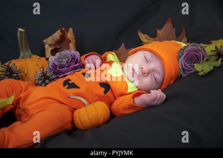 Surrey, UK, 28th October, 2018. A sleeping six week old male Caucasian baby boy, peacefully asleep, is dressed in an orange all-in-one babygrow with a Halloween theme pumpkin design, surrounded by pumpkins, gourds and fallen leaves appropriate to the autumnal occasion. Credit: Graham Prentice/Alamy Live News Stock Photo