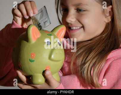 Sieversdorf, Germany. 29th Oct, 2018. Illustration: A girl puts a 5-euro bill in a piggy bank. 30.10. is World Savings Day. Credit: Patrick Pleul/dpa-Zentralbild/ZB/dpa/Alamy Live News Stock Photo