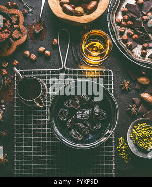 Soaked in rum prunes for homemade pralines with various chocolate, spices and nuts ingredients on dark table background with vintage kitchen utensils, Stock Photo