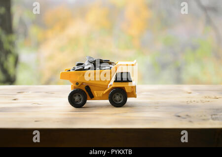 A small yellow toy truck is loaded with sunflower seeds. A car on a wooden surface against a background of autumn forest. Extraction and transportatio Stock Photo