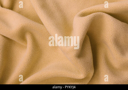 The blanket of furry orange fleece fabric. A background of light orange soft plush fleece material with a lot of relief folds Stock Photo