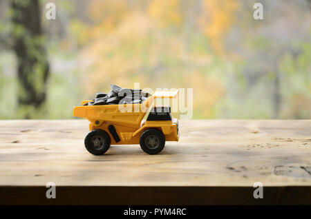 A small yellow toy truck is loaded with sunflower seeds. A car on a wooden surface against a background of autumn forest. Extraction and transportatio Stock Photo