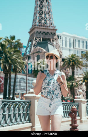 young backpacker walking next to the tall tower. beautiful lady tourist with hat and sunglasses travel in las vegas in summer. woman traveler having v Stock Photo