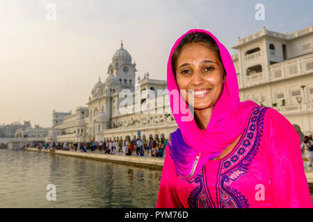 A portrait of a smiling young female Sikh devotee, dressed in red cloths, inside the Harmandir Sahib, the Golden Temple, complex Stock Photo