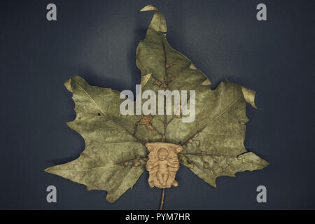 Baby Jesus Christ in the manger on a dry leaf isolated on black background. Christmas Nativity Scene figure. Stock Photo