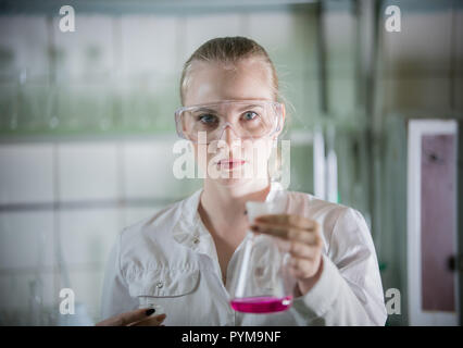 Chemical laboratory. Young blonde woman holding a flask with liquid in it Stock Photo