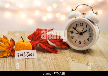 Fall Back Daylight Saving Time concept with white clock and autumn leaves, soft bokeh background on wooden board Stock Photo
