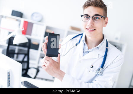 A young man in a white robe standing in the office and holding a phone. Stock Photo