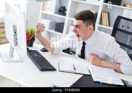 A young man sitting at a computer Desk in the office and shows his fist in the monitor. Stock Photo