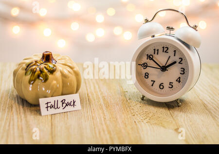 Fall Back Daylight Saving Time concept with white clock and autumn leaves, soft bokeh background on wooden board Stock Photo