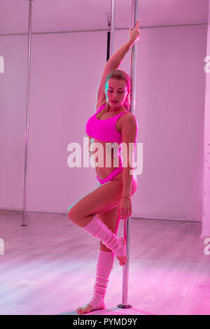 Slim athletic dancer wearing bright pink sport suit standing near pole Stock Photo