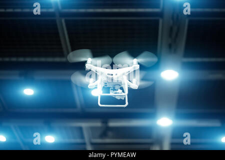 White drone in motion. Quadcopter flying inside a large warehouse Stock Photo