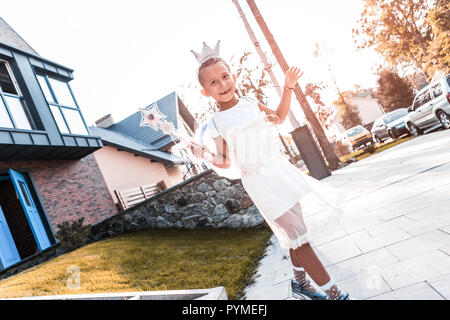 Cute little girl wearing crown and holding magic wand walking in the street Stock Photo