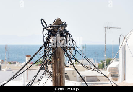 Old traditional electric distribution wood pole with a tangle of power cables in a town on an Aegean island, Greece Stock Photo