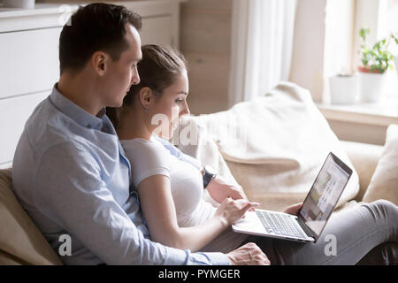 Millennial couple sitting on couch using laptop Stock Photo