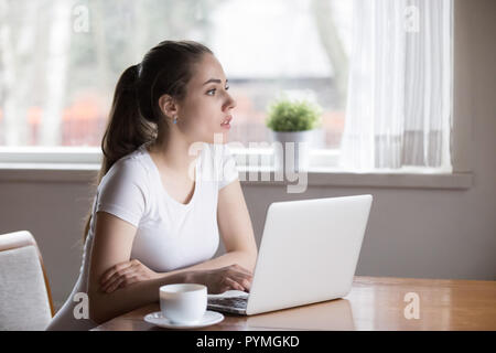 Serious pensive woman using laptop sitting in the kitchen Stock Photo