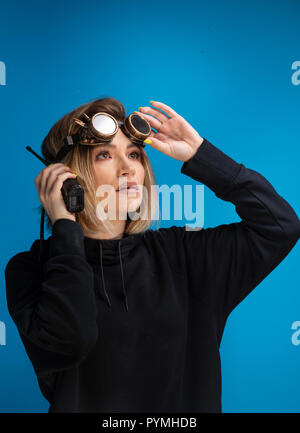 Portrait of dark blonde girl with steam punk glasses using a walkie talkie communication device. Posing looking up at the right corner Stock Photo