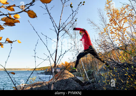 Bearded man in red shirt running near the lake at autumn time. Trail running concept Stock Photo