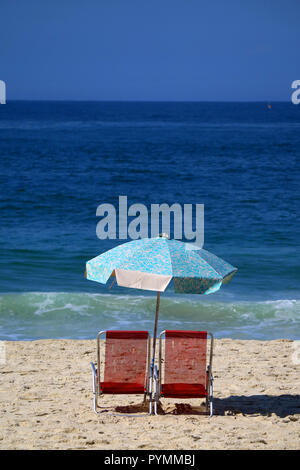 Vertical photo of a pair of red beach chairs and light blue parasol on the sandy beach against vivid blue Atlantic ocean Stock Photo