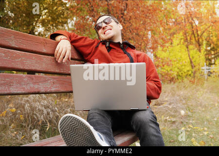 young man entrepreneur celebrating business success reading good news on laptop in park. Guy freelancer laughs holding ultrabook in hand. Worker in ca Stock Photo