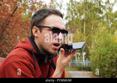 Recording on dictaphone. leisure, technology, communication and people concept - hipster man using voice command recorder or calling on smartphone at  Stock Photo