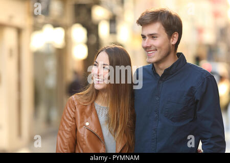 Happy couple dating walking in the street of an old town looking at side Stock Photo