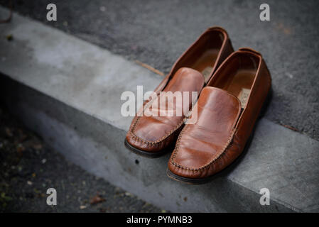 Shiny brown leather shoes left out on the concrete pavement Stock Photo