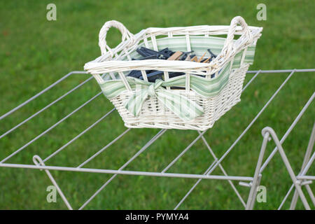 White wicker basket of clothes pegs on a wire drying stand. Stock Photo