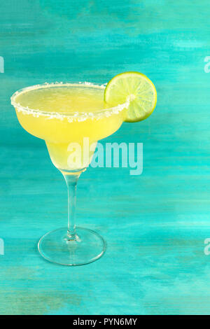 A photo of a lemon Margarita cocktail in the traditional glass with a wedge of lime on a vibrant teal background with a place for text Stock Photo