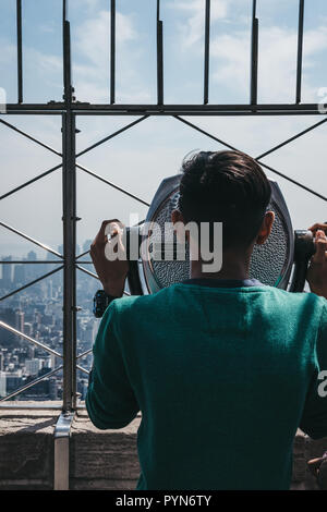 New York, USA - May 29, 2018: Young man looking using binoculars on the observation platform at Empire State Building, New York. New York is one of th Stock Photo