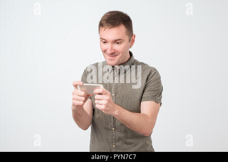 Close up portrait of a funny young positive man playing games on his smart phone Stock Photo