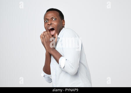 Puzzled african man isolated on grey background dressed in white shirt, covering mouth with hands Stock Photo