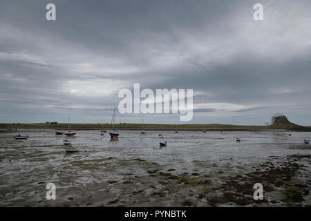 The Ouse with anchored boats at low tide from Willy Pots Rock on Holy Island with Lindesfarne Castle under renovation England UK Stock Photo