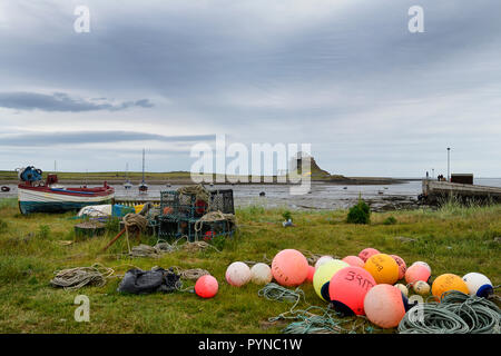 Bright fishing bouys and lobster pots on shore at The Ouse bay on Holy Island with Lindisfarne Castle under renovation England UK Stock Photo
